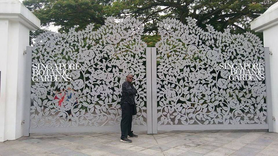 Joel Crafton, known as Black Pinoy, standing in front of the Singapore Botanic Gardens during his international travels.