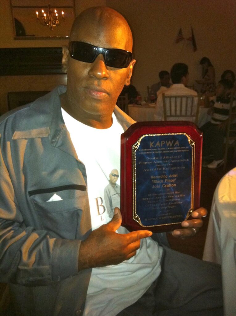 Internationally recognized celebrity recording artist Black Pinoy Joel Crafton holding a plaque of recognition honoring his contributions to music, culture, entertainment, and the Filipino community.